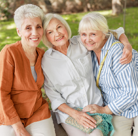 three elderly women smiling for the camera with their arms around one another