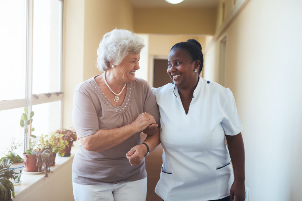 senior lady walking with a caregiver in a hallway